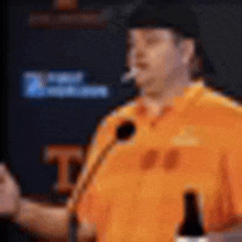 a man in an orange shirt is speaking into a microphone