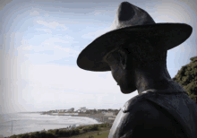 a statue of a man wearing a hat is looking out over the water