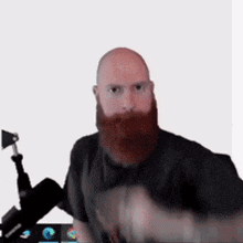 a bald man with a red beard is sitting in front of a microphone and looking at the camera .