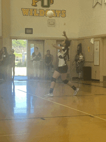 a girl playing volleyball in front of a wall with the word wildcats on it