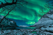 the aurora borealis is visible over a snowy mountain range and a lake