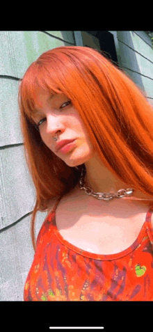 a woman with red hair and a nose ring is wearing a red tank top and a necklace .