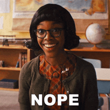 a woman wearing glasses and a green cardigan is smiling with the word nope behind her