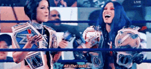 two women are standing in a wrestling ring holding their championship belts and laughing .