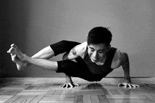 a black and white photo of a man doing yoga on a wooden floor