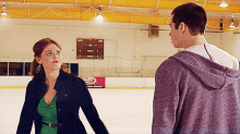 a man and a woman are standing on an ice rink in front of a sign that says ' coca cola '