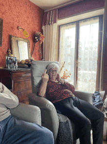 an elderly woman sits in a chair and shows the middle finger