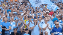 a crowd of people standing in a stadium applauding and holding up flags .