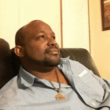 a man with a beard is sitting on a couch wearing a blue shirt and tie .