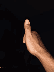 a man 's hand is giving a thumbs up in the dark