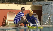 a man in a striped shirt is kneeling next to a man in a costume cleaning a swimming pool .