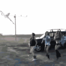 a group of women are dancing in front of a car while a kite is flying in the background .