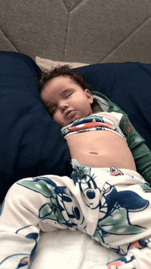 a baby sleeping on a bed with a mickey mouse blanket