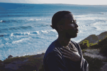 a man with his hands on his chest looking out over the ocean