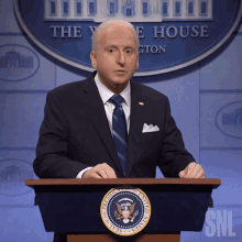 a man in a suit and tie stands at a podium with the seal of the president of the united states on it