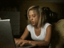 a woman in a white shirt is typing on a laptop