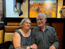 a man and a woman are posing for a picture in front of a painting of a canyon