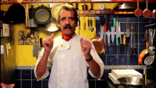 a man in a chef 's uniform is giving a thumbs up in front of a wall of kitchen utensils