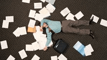 a man is laying on the floor surrounded by papers and a bag .