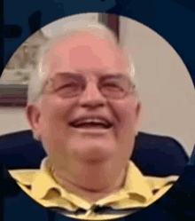 an older man wearing glasses and a yellow shirt is smiling .