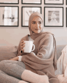 a woman in a hijab sits on a couch holding a cup