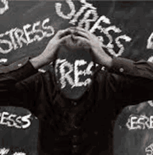 a man is covering his face in front of a blackboard with the word stress written on it .