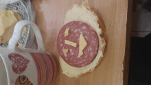 a sandwich with a smiley face on it sits next to a cup with hearts on it