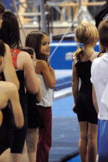 a group of young girls are standing in a gym and one of them is wearing a black leotard