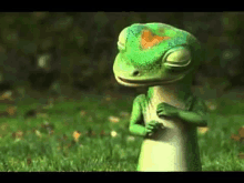 a green lizard is standing in the grass with his eyes closed .