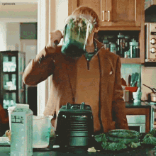 a man in a brown jacket is drinking from a blender in a kitchen with a bottle of milk on the counter