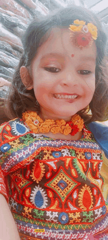 a little girl wearing a necklace and a flower in her hair is smiling .