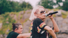 a woman is singing into a microphone while wearing sunglasses and a black shirt that says ' reggae ' on it