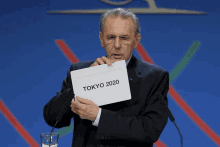 a man in a suit holds a sign that says tokyo 2020