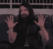 a man with long hair and a beard holds up his hands in front of a row of blue seats