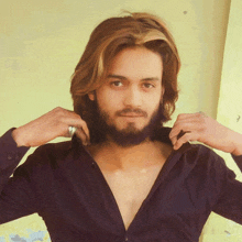 a young man with long hair and a beard is adjusting his shirt