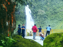 a group of people standing in front of a waterfall with one wearing a shirt that says ' a ' on the back