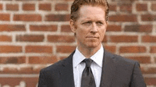 the man is wearing a suit and tie and is standing in front of a brick wall .