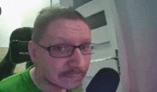 a man with glasses and a mustache is sitting in front of a microphone and making a funny face .