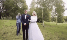 a bride and groom are posing for a picture in a park while a photographer takes a picture of them .