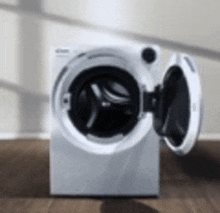 a white washing machine with its door open is sitting on a wooden floor in a room .