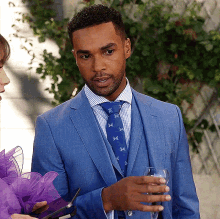 a man in a blue suit and tie is holding a glass of wine while talking to a woman .