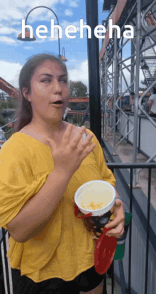 a woman in a yellow shirt is holding a cup of popcorn and laughing with the word heneheneha above her