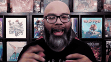 a bald man with glasses and a beard stands in front of a shelf full of books including the isle of cats