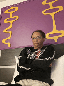 a woman wearing a black shirt with a skeleton on it is sitting on a bed