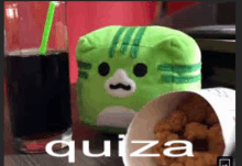 a green stuffed animal sitting next to a cup of chicken nuggets and a glass of soda