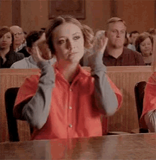 a woman in an orange shirt is sitting at a table in a courtroom with her hands on her head .