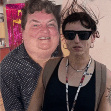 a woman wearing sunglasses stands next to a man wearing a lanyard that says " i love you "