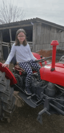 a young girl is sitting on a red tractor in front of a barn