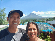 a man and woman pose for a picture in front of a mountain