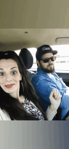 a man and a woman are sitting in a car and the man is wearing a hat that says " daddy " on it